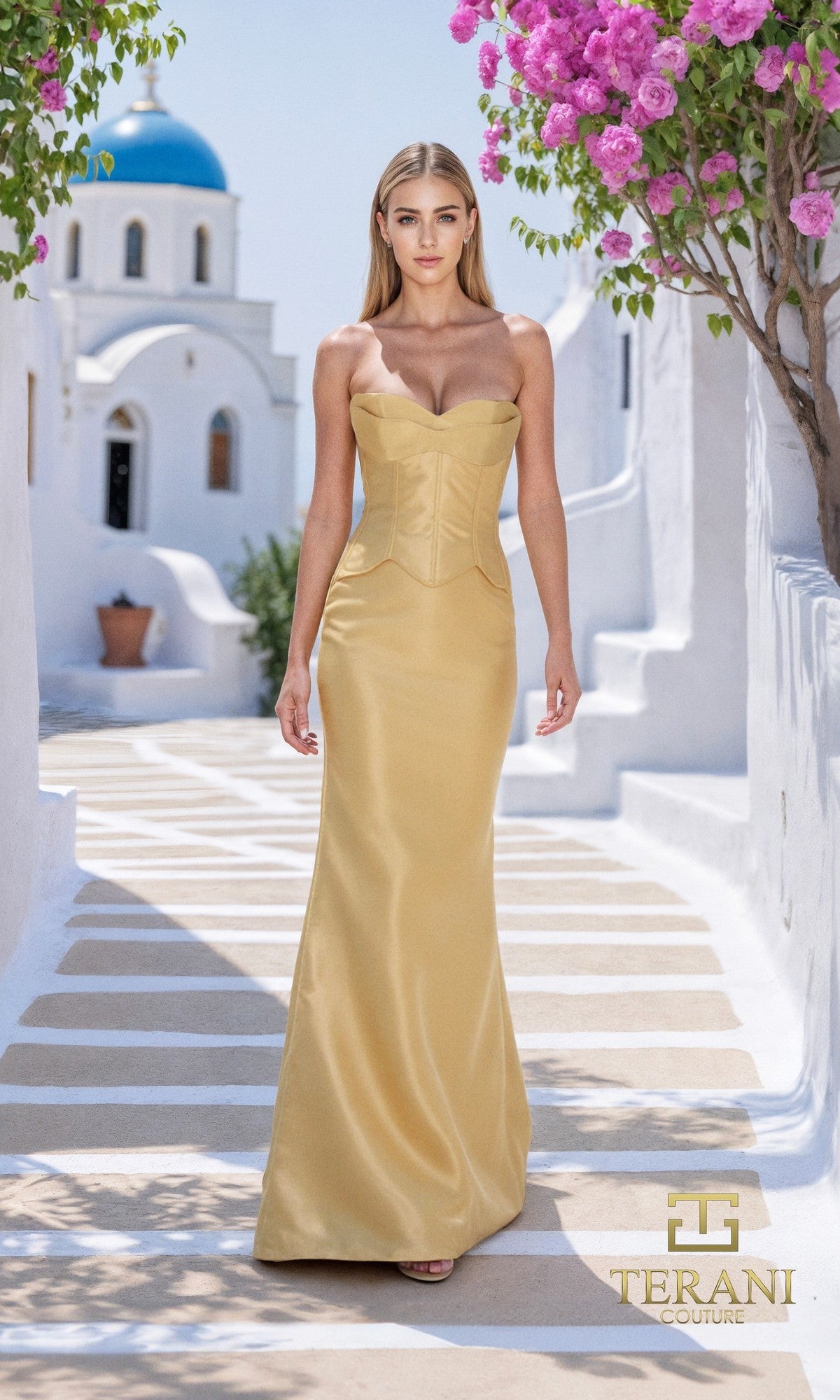 A woman in a gold, strapless long formal dress (Terani 261E6292) with a sheath silhouette stands on a sunlit path lined with white buildings and pink flowers; the Terani Couture logo appears at the bottom right.